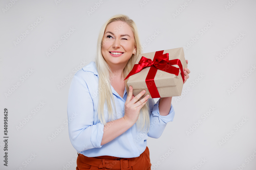 valentine's day or christmas concept - portrait of surprised beautiful and elegant plus size blonde woman holding gift box over gray valentine's day or christmas concept - portrait of surprised beautiful and elegant plus size blonde woman holding gift box over gray