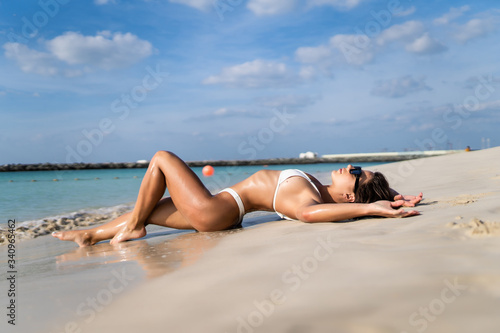Young relaxing woman in white bikini lying on the sand on the beach