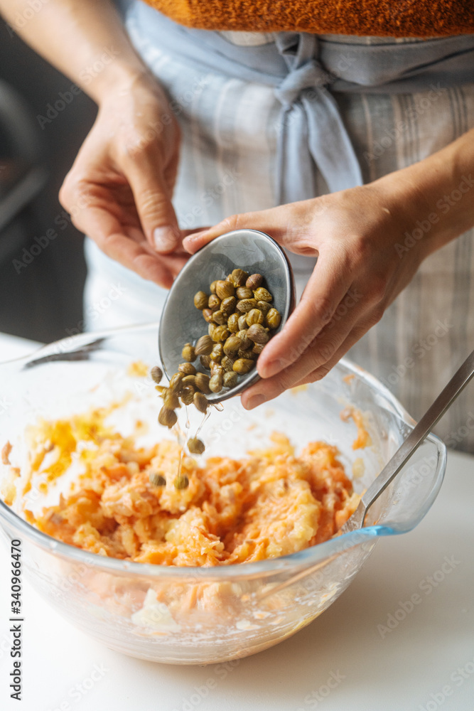 Crop female adding marinated capers into transparent glass bowl with salmon stuffing while preparing healthy dinner at home kitchen Crop female adding marinated capers into transparent glass bowl with salmon stuffing while preparing healthy dinner at home kitchen