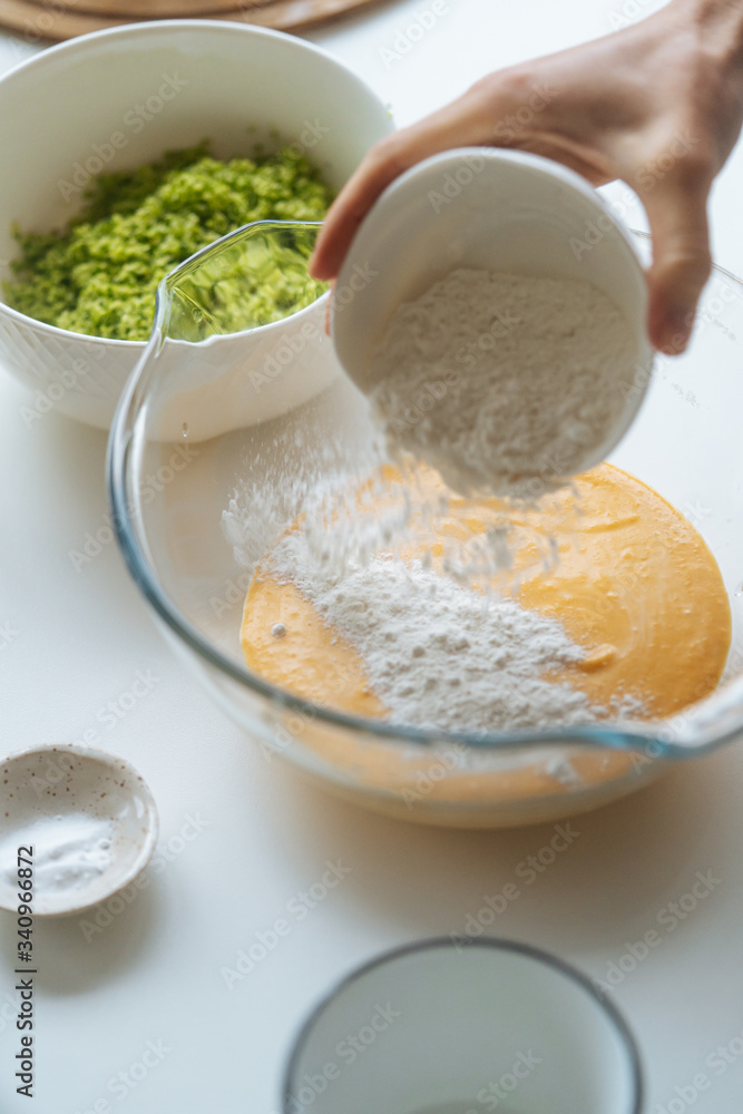From above cook carefully pouring flour into glass bowl with orange vegetable mixture on table in light kitchen From above cook carefully pouring flour into glass bowl with orange vegetable mixture on table in light kitchen