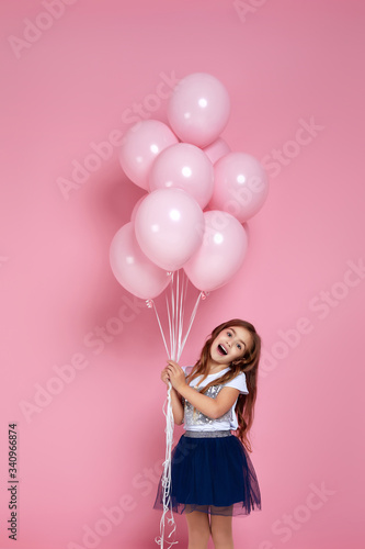 Smiling adorable little child girl posing with pastel pink air balloons isolated over pink background. Beautiful happy kid on a birthday party.