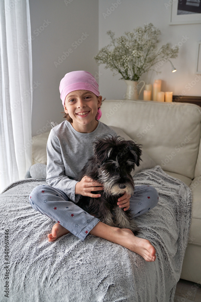 From above adorable sick little boy in pink bandana and pajama caressing pet while sitting on bed at home looking at camera From above adorable sick little boy in pink bandana and pajama caressing pet while sitting on bed at home looking at camera
