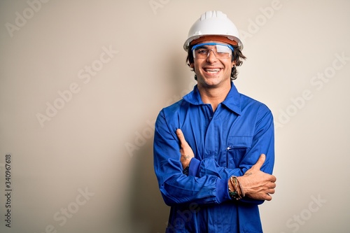 Young constructor man wearing uniform and security helmet over isolated white background happy face smiling with crossed arms looking at the camera. Positive person. photo