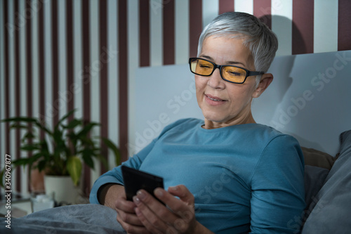 Canvas-taulu Senior Woman with Blue Light Blocking Glasses Using Smartphone in the Evening