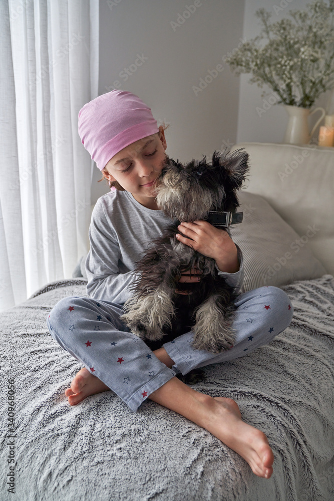From above adorable sick little boy in pink bandana and pajama caressing pet while sitting on bed at home From above adorable sick little boy in pink bandana and pajama caressing pet while sitting on bed at home
