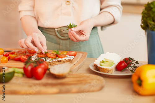 Warm-toned close up of unrecognizable woman preparing healthy tomato sandwiches for breakfast in cozy kitchen interior, copy space