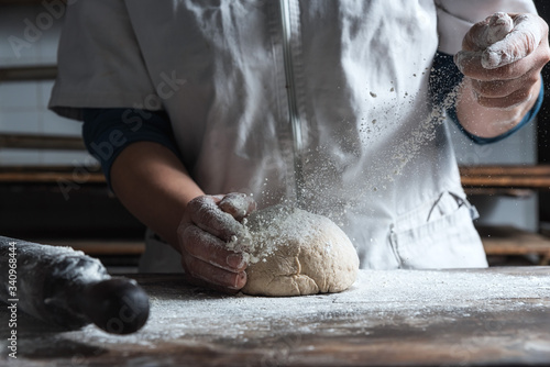 Unrecognizable person kneading dough with flour on table while working in bakery photo
