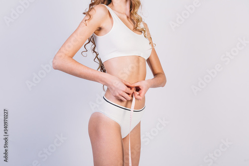 young slim girl in white sportswear measures her waist with a centimeter