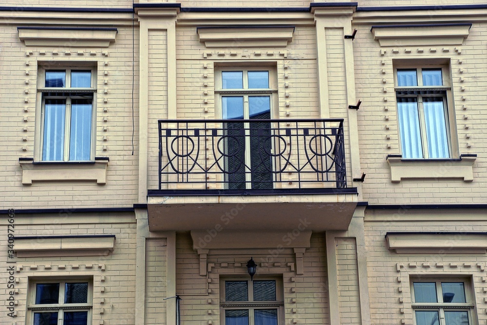 Obraz premium jeden otwarty balkon z czarnego żelaza z kutym wzorem na brązowej ceglanej ścianie z oknami i szklanymi drzwiami od ulicy