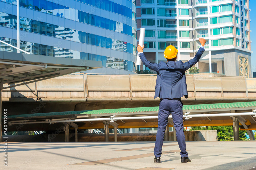 Project successful. Engineer celebrating his victory with arms up on cityscape background. Project successful. Engineer celebrating his victory with arms up on cityscape background.