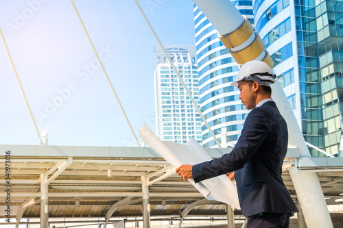 Engineer with helmet looking paper plans at construction site.