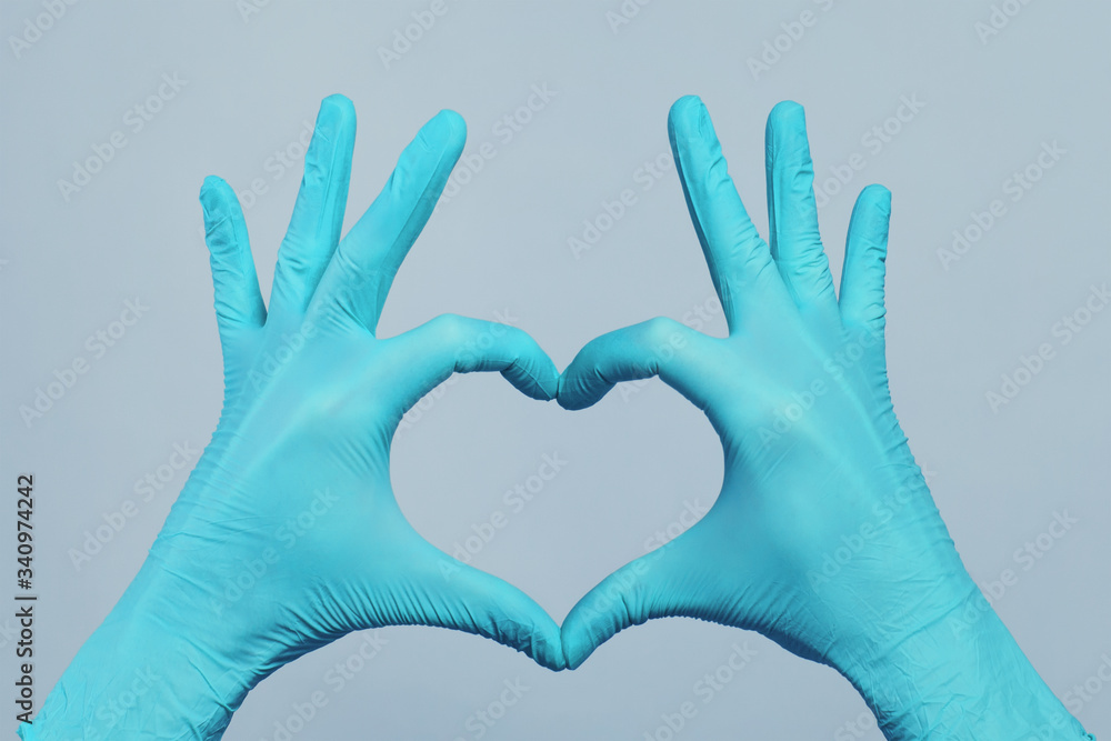 Fototapeta premium Hands in blue doctor gloves making heart on gray background. Medical assistance concept