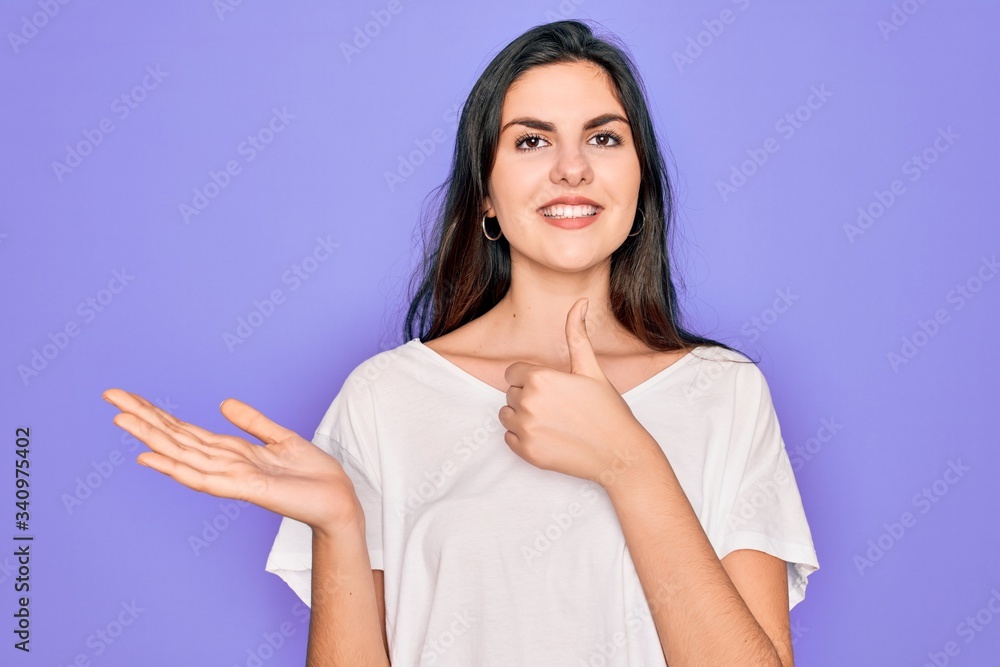 Obraz premium Young beautiful brunette woman wearing casual white t-shirt over purple background Showing palm hand and doing ok gesture with thumbs up, smiling happy and cheerful