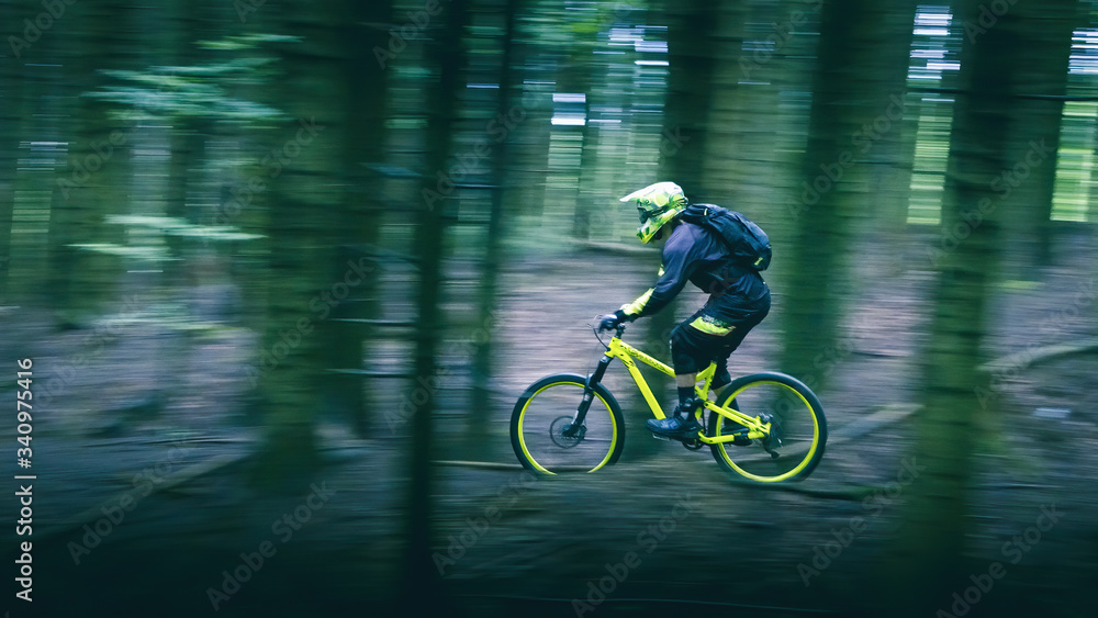 Man in full face helmet on the yellow enduro bicycle with backpack very fast rides in the forest. Trees was blurred high speed Man in full face helmet on the yellow enduro bicycle with backpack very fast rides in the forest. Trees was blurred high speed