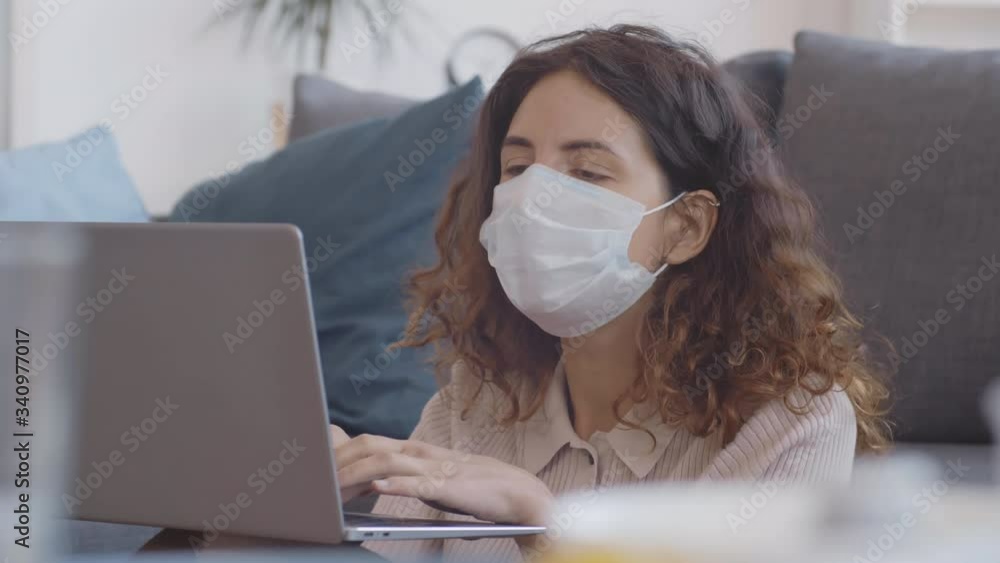 Close up of pretty young woman wearing medical mask staying home and working on laptop. Then she is having online video call Close up of pretty young woman wearing medical mask staying home and working on laptop. Then she is having online video call
