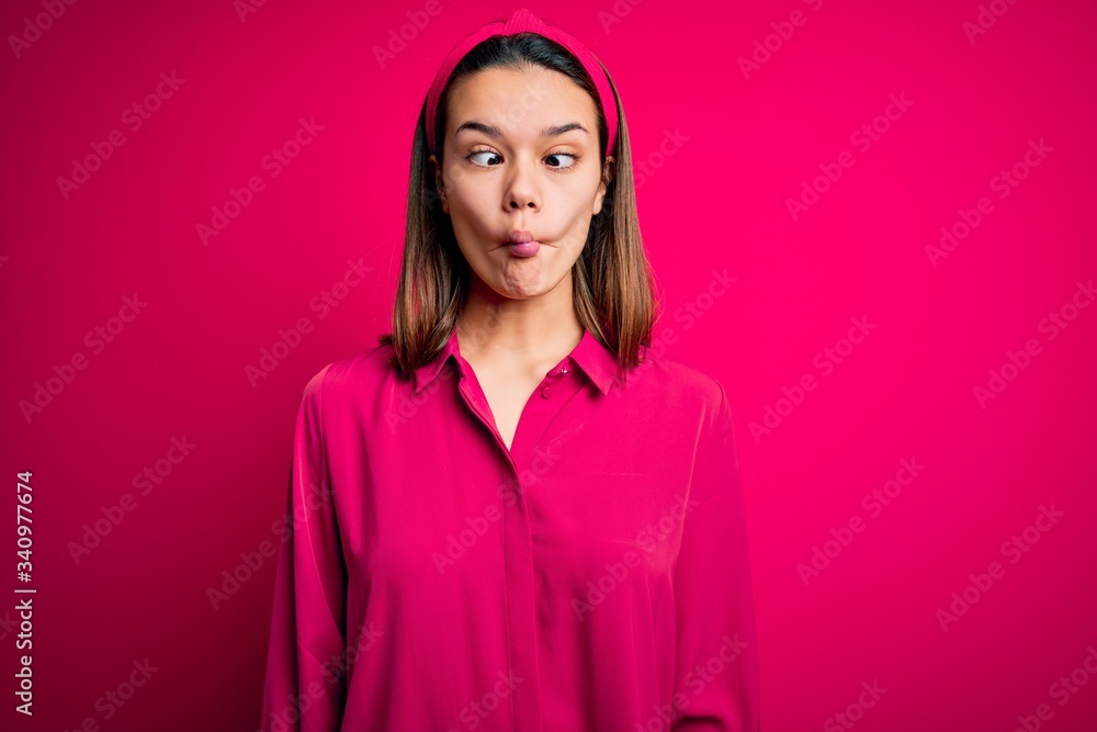 Fototapeta premium Young beautiful brunette girl wearing casual shirt standing over isolated pink background making fish face with lips, crazy and comical gesture. Funny expression.