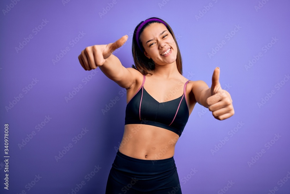 Young beautiful sporty girl doing sport wearing sportswear over isolated purple background approving doing positive gesture with hand, thumbs up smiling and happy for success. Winner gesture. Young beautiful sporty girl doing sport wearing sportswear over isolated purple background approving doing positive gesture with hand, thumbs up smiling and happy for success. Winner gesture.