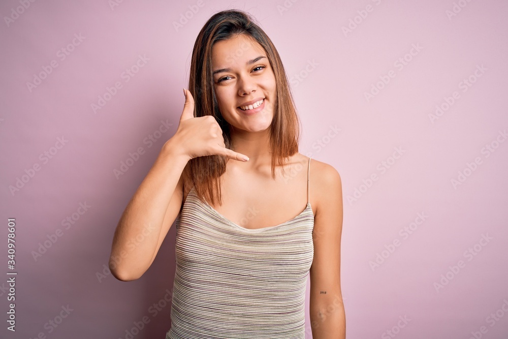 Young beautiful brunette girl wearing casual striped t-shirt over isolated pink background smiling doing phone gesture with hand and fingers like talking on the telephone. Communicating concepts. Young beautiful brunette girl wearing casual striped t-shirt over isolated pink background smiling doing phone gesture with hand and fingers like talking on the telephone. Communicating concepts.
