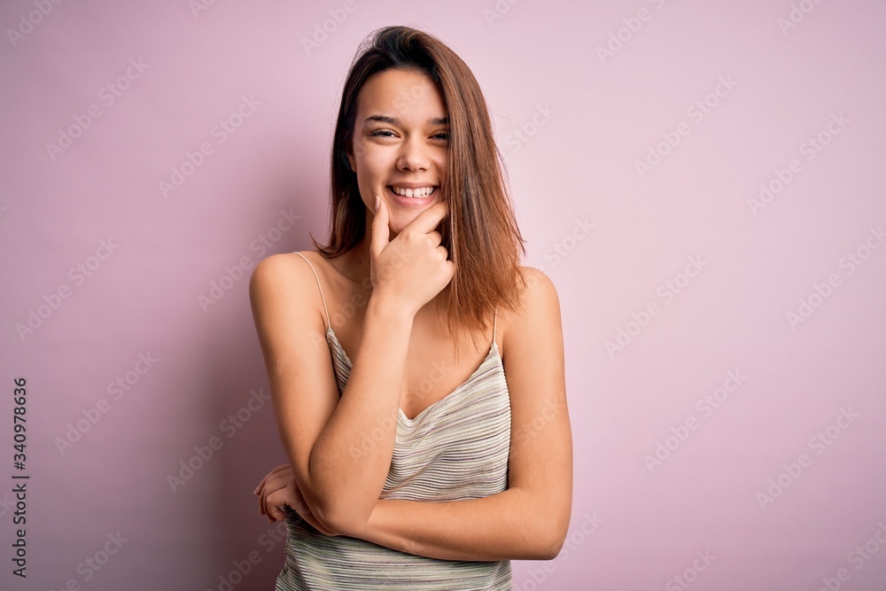 Young beautiful brunette girl wearing casual striped t-shirt over isolated pink background looking confident at the camera smiling with crossed arms and hand raised on chin. Thinking positive. Young beautiful brunette girl wearing casual striped t-shirt over isolated pink background looking confident at the camera smiling with crossed arms and hand raised on chin. Thinking positive.