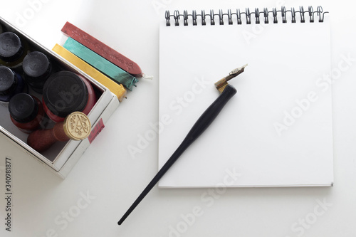 Pen for calligraphy next to paper and ink on a white background