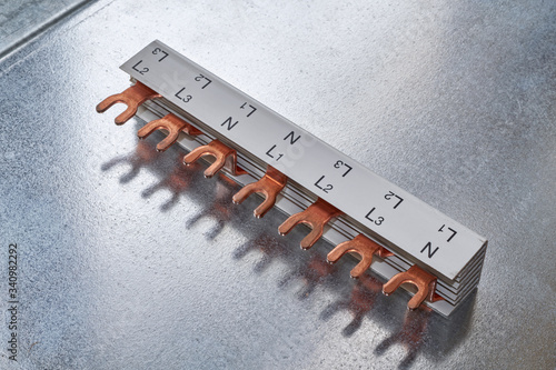 The busbar made of copper with a cutout in the form of a plug for modular electric switches lies on a metal sheet. The busbar is insulated in a special dielectric plastic or material.
