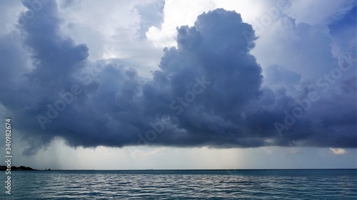 Waiting for a thunderstorm. Maldives. A large dark blue cloud hung over the ocean. The ocean is calm. An island is visible in the distance. Everything is quiet.