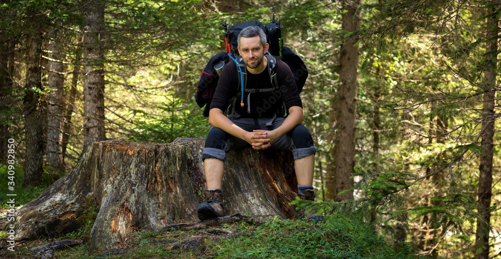 A man sitting with a backpack on a tree trunk by the trail