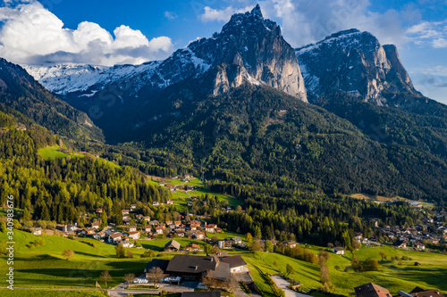 Aerial view of improbable green meadows of Italian Alps, green slopes of the mountains, Bolzano, huge clouds over a valley, roof tops of houses, Dolomites on background, sunshines through clouds © Vladimir Drozdin