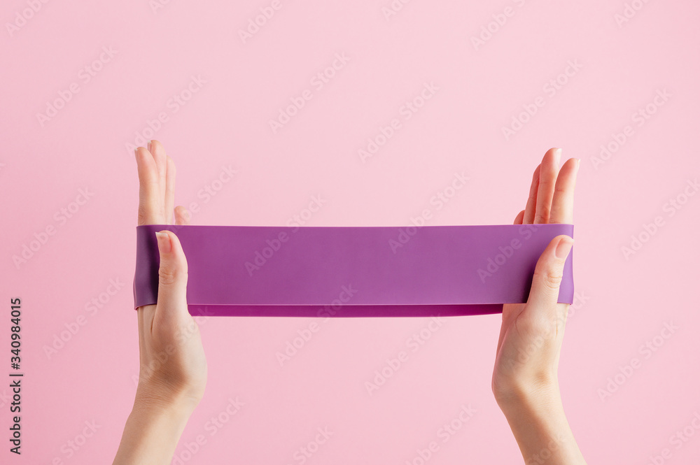 Woman stretch fitness band. Violet rubber for home exercises. Indoor and outdoor workout. Sport and healthy active lifestyle concept. Isolated on pink background