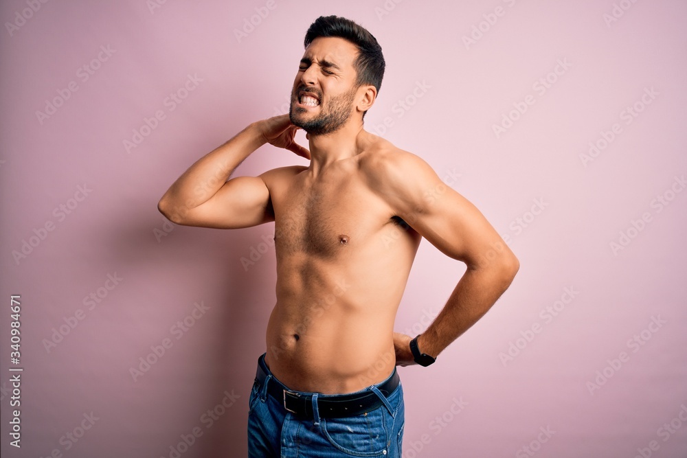 Fototapeta premium Young handsome strong man with beard shirtless standing over isolated pink background Suffering of neck ache injury, touching neck with hand, muscular pain