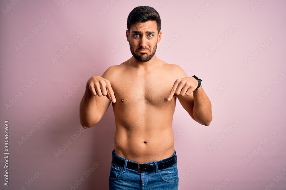 Young handsome strong man with beard shirtless standing over isolated pink background Pointing down looking sad and upset, indicating direction with fingers, unhappy and depressed.