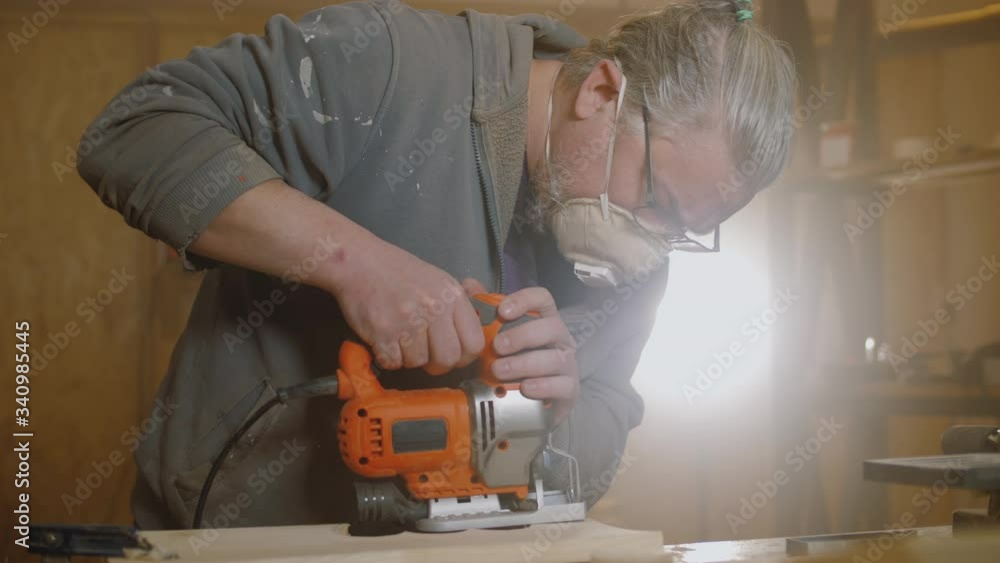 Carpenter uses electric jigsaw to cut wooden board, wood craftsman working Carpenter uses electric jigsaw to cut wooden board, wood craftsman working