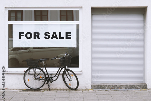 for sale sign in store window with bicycle parked outside - shop vacancy due to business closure - economy crisis and recession concept