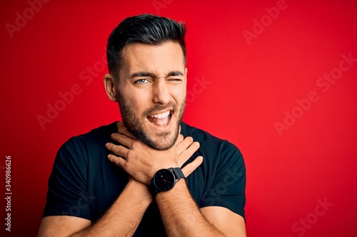 Young handsome man wearing casual black t-shirt standing over isolated red background shouting and suffocate because painful strangle. Health problem. Asphyxiate and suicide concept.