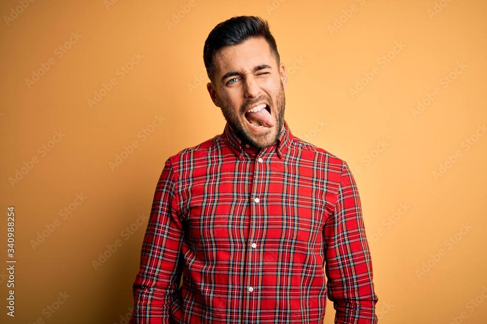 Fototapeta premium Young handsome man wearing casual shirt standing over isolated yellow background sticking tongue out happy with funny expression. Emotion concept.