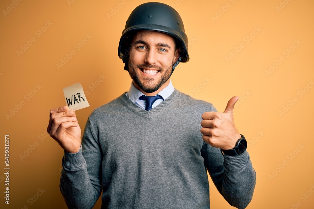 Handsome businessman wearing military helmet holding reminder paper with war message happy with big smile doing ok sign, thumb up with fingers, excellent sign Handsome businessman wearing military helmet holding reminder paper with war message happy with big smile doing ok sign, thumb up with fingers, excellent sign