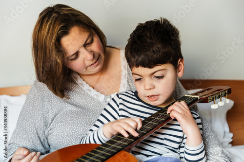 niño juega y aprende con una mujer a tocar la guitarra en la cama. son madre e hijo, él tiene una pluridiscapacidad. Actividad sensorial. están alegres y riendo. instrumento de música. educación.