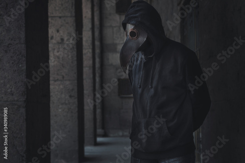 Dark horror figure in black hood in plague doctor mask on the grunge background. Stylized epidemic costume