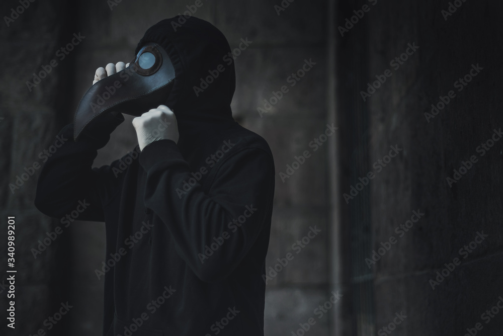 Dark horror figure in black hood in plague doctor mask on the grunge background. Stylized epidemic costume Dark horror figure in black hood in plague doctor mask on the grunge background. Stylized epidemic costume
