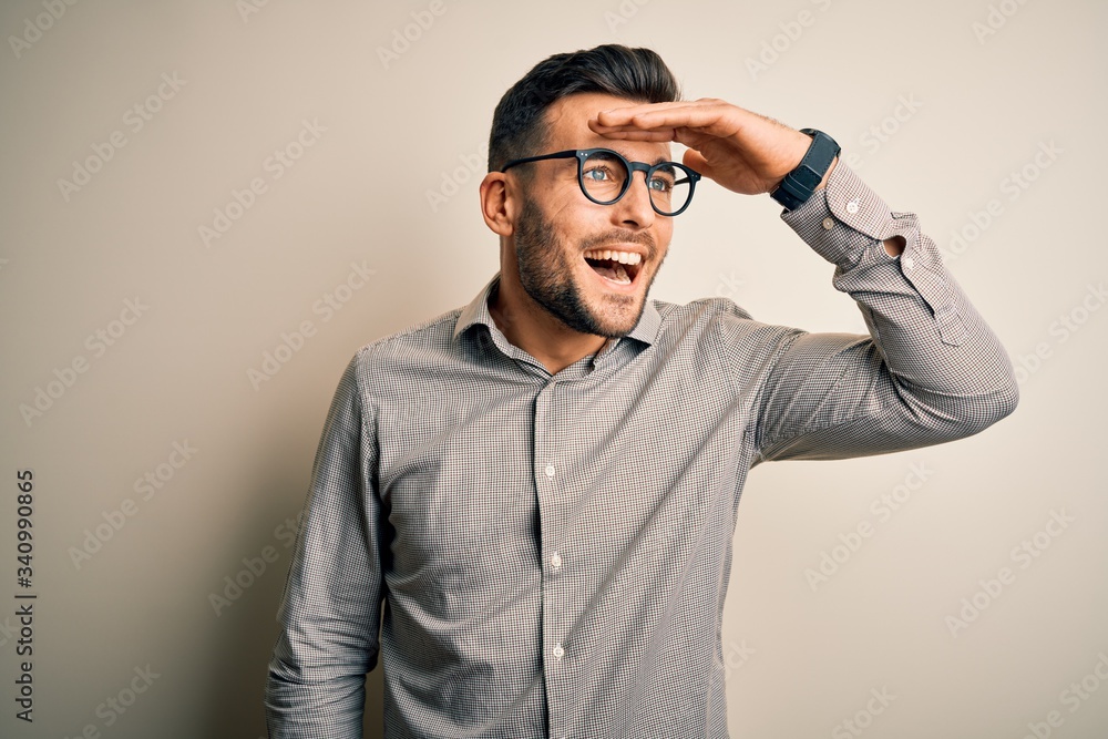 Young handsome man wearing elegant shirt and glasses over isolated white background very happy and smiling looking far away with hand over head. Searching concept. Young handsome man wearing elegant shirt and glasses over isolated white background very happy and smiling looking far away with hand over head. Searching concept.
