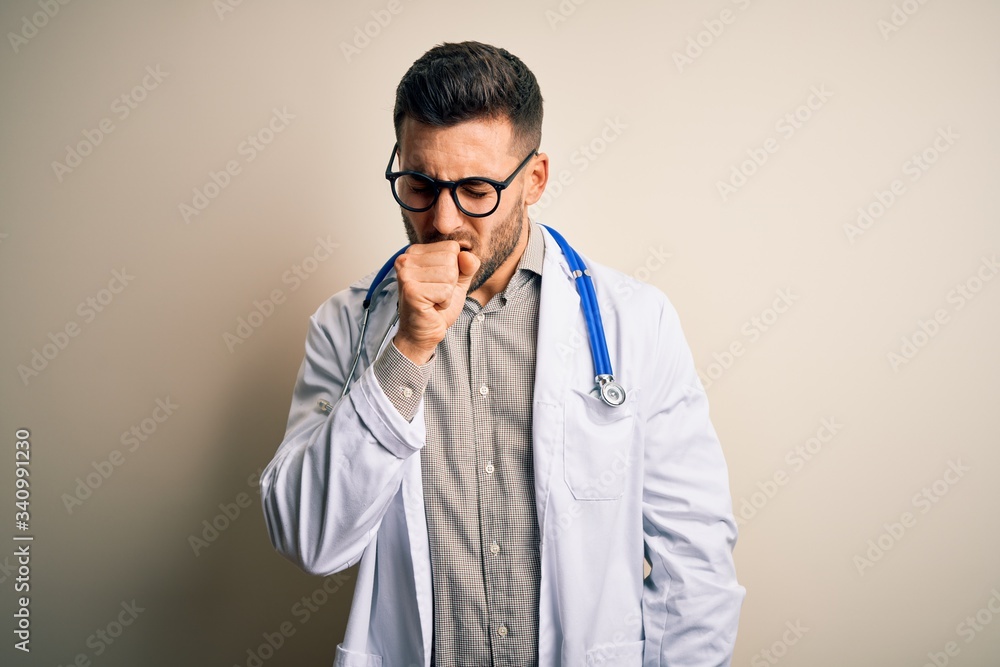 Young doctor man wearing glasses, medical white robe and stethoscope over isolated background feeling unwell and coughing as symptom for cold or bronchitis. Health care concept. Young doctor man wearing glasses, medical white robe and stethoscope over isolated background feeling unwell and coughing as symptom for cold or bronchitis. Health care concept.