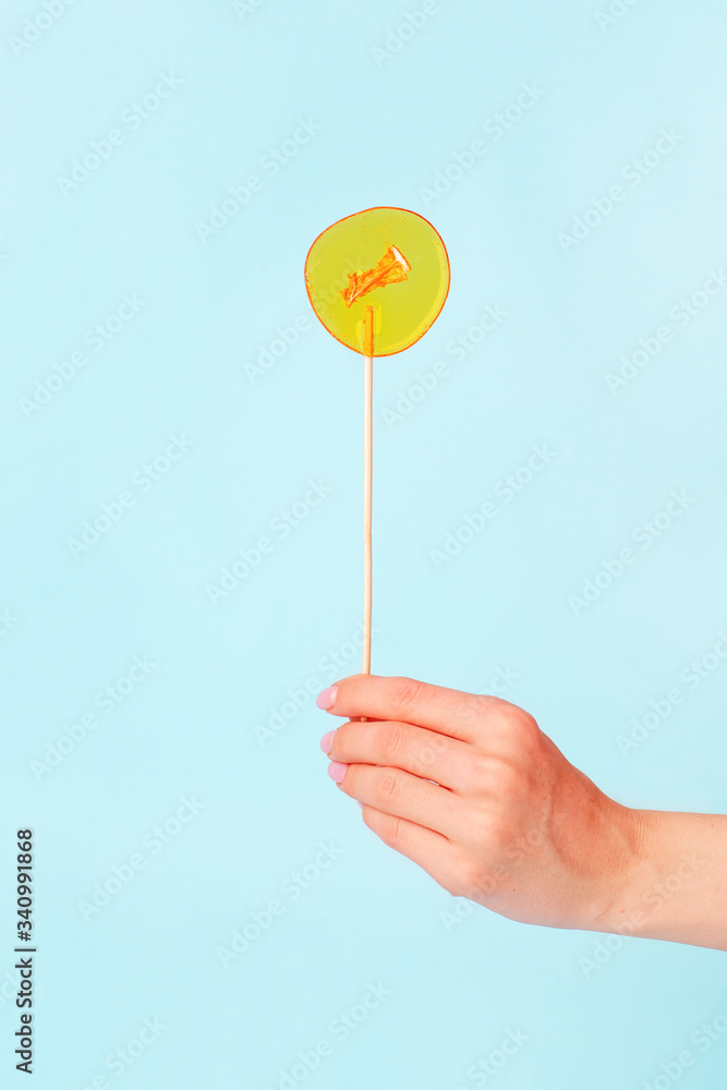 Yellow lollipop in woman hand on blue background. Girls hold hard candy caramel on stick, sweets holidays concept, copy space for text, minimal, summer creative idea - sun and blue sky Yellow lollipop in woman hand on blue background. Girls hold hard candy caramel on stick, sweets holidays concept, copy space for text, minimal, summer creative idea - sun and blue sky