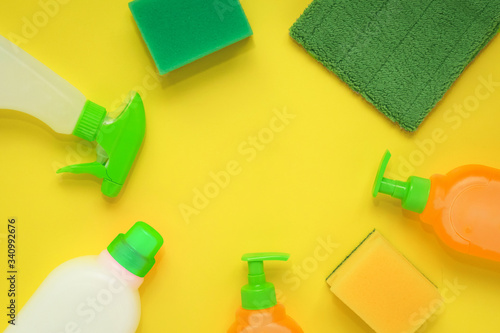 flat on a bright yellow background, household cleaning products, bottles, sprays, sponges for dishes and a rag 