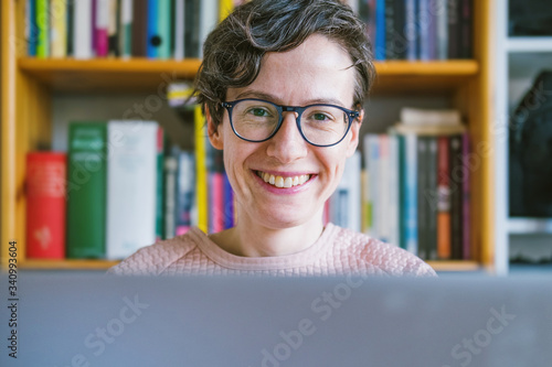 Working remote from home office. Young Caucasian short hair entrepreneur woman with glasses working from home on computer laptop, looking over monitor and smiling