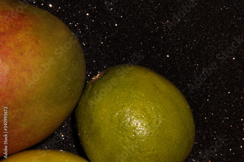 Fruit on a black shiny background. Green fruit on a black background. Mango red-green and lime.