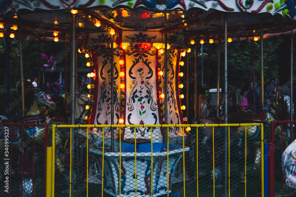 Children's carousel with burning lights and fenced with a metal fence