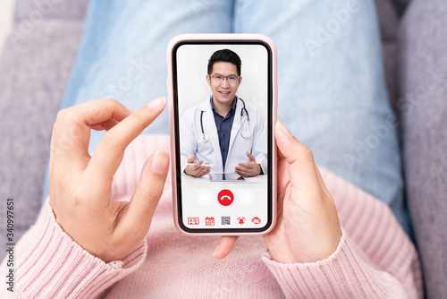 Asian chinese doctor or therapist help releave stress from coronavirus crisis video conference call online live talk remotely with woman sit on sofa couch at home using smartphone doctor consultation. photo