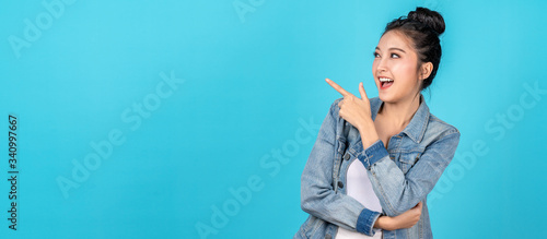 Banner of Happy asian woman standing pointing hands to copyspace on blue background. Cute asia girl smiling wearing casual jeans shirt and finger pointing to aside for present promotions.