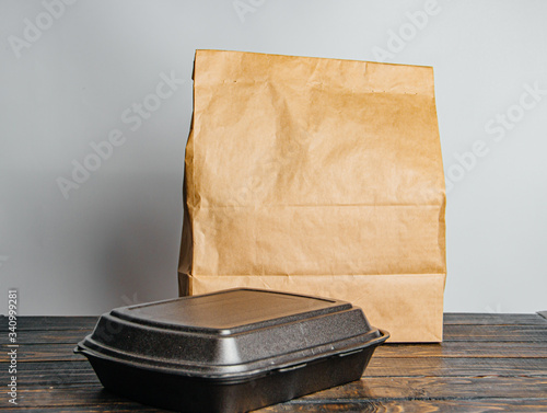 Tablou pe pânză A brown craft paper bag and a black container for taking out or delivering goods and food on a wooden table
