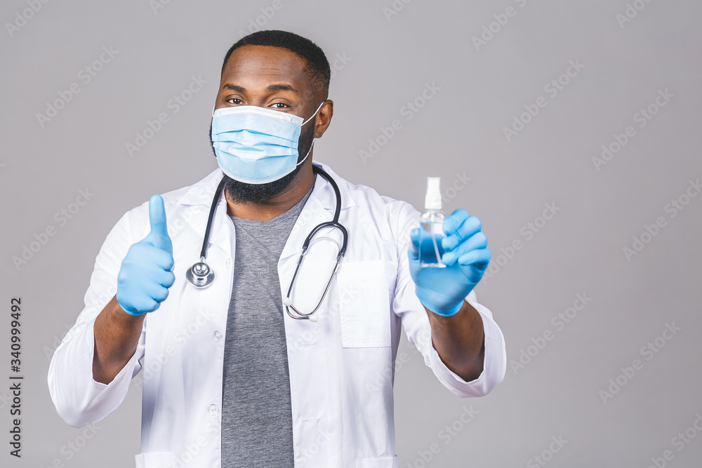 African american doctor man in gown face mask gloves isolated on grey background. Epidemic pandemic coronavirus 2019-ncov sars covid-19 flu virus. Holding bottle liquid antibacterial sanitizer.